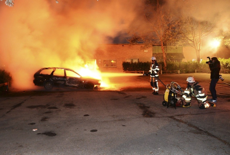 Firefighters extinguish a burning car, following riots in the Stockholm suburb of Kista (Reuters)