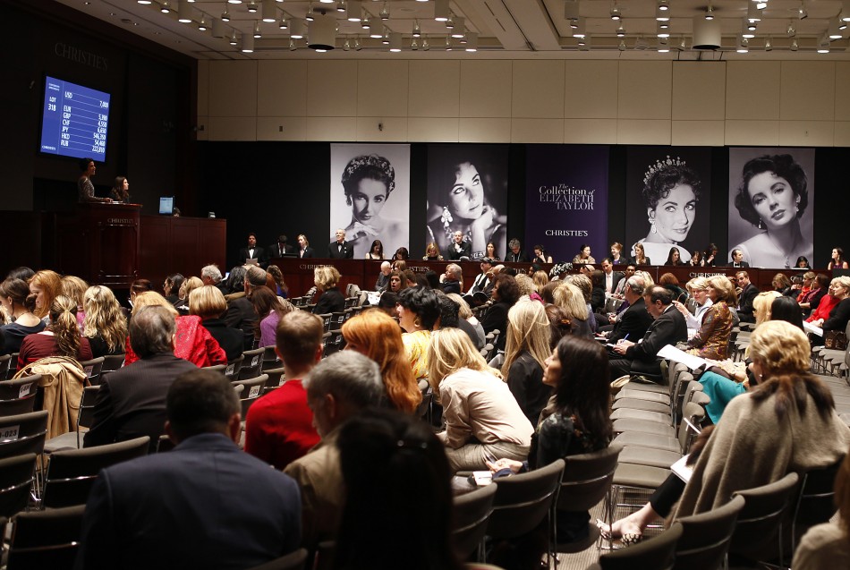 People sit near images of Elizabeth Taylor during an auction of the late actress jewelry, clothing, art and memorabilia at Christies auction house