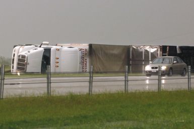 A car passes two semi tractor-trailers, flipped by a tornado, along Interstate-40 eastbound