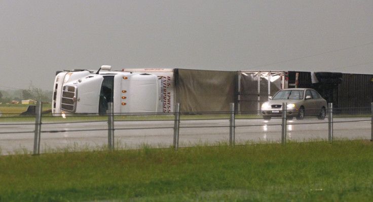 A car passes two semi tractor-trailers, flipped by a tornado, along Interstate-40 eastbound