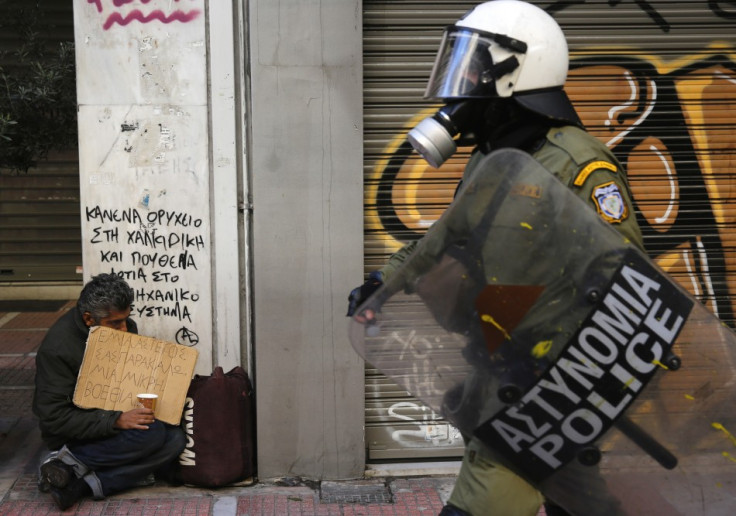 A riot policeman walks by a homeless beggar during a rally in Greece (Photo: Reuters)