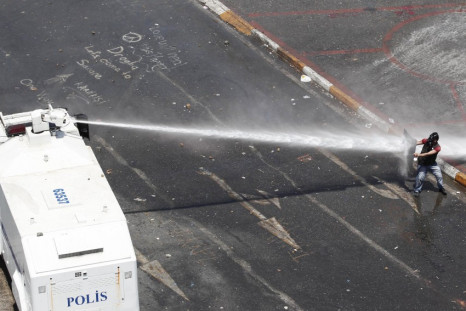 A protester holding a shield attempts to block a jet of water from a police water cannon