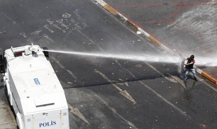 A protester holding a shield attempts to block a jet of water from a police water cannon