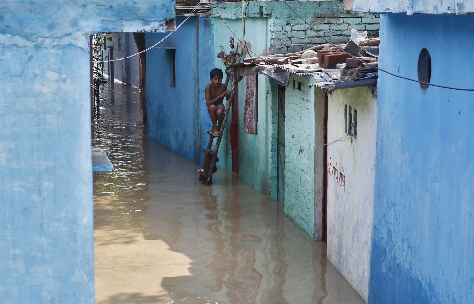 A boy sits on a ladder next to his flooded house with the rising water level of river Yamuna after heavy monsoon rains in New Delhi June 19, 2013