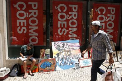 A man walks past a painter selling his work in front of a shop announcing promotions during the general strike in Lisbon June 27, 2013. (Photo: Reuters)