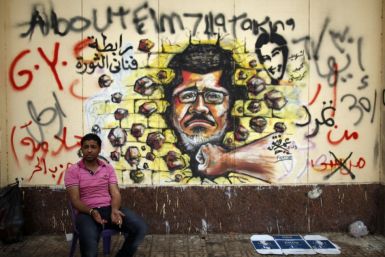 A protester, opposing Egypt's President Mohamed Morsi, sits next to graffiti depicting Morsi on a wall of the Presidential Palace (Reuters0