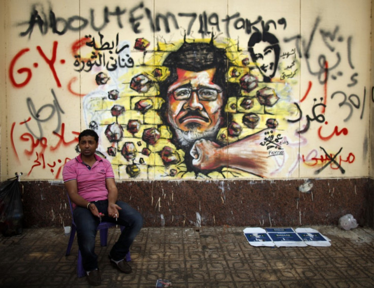 A protester, opposing Egypt's President Mohamed Morsi, sits next to graffiti depicting Morsi on a wall of the Presidential Palace (Reuters0