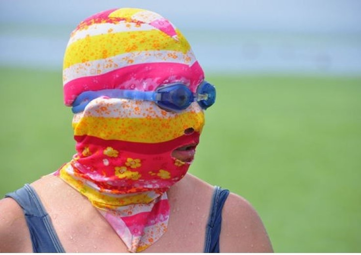 A woman wearing “facekinis” chill out at beach floated with enteromorpha prolifera in Qingdao.