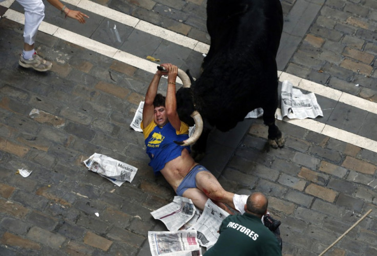 A runner holds on to the horn of an El Pilar fighting bull, after being gored by it, on Estafeta street during the sixth running of the bulls of the San Fermin festival (Reuters)