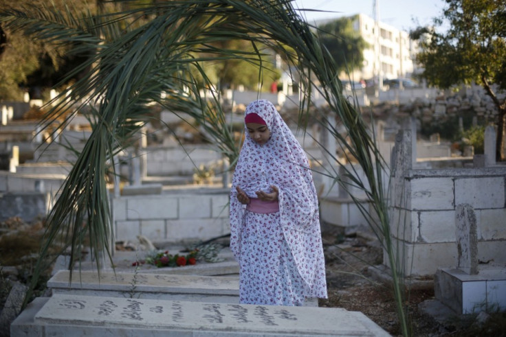 A Palestinian girl prays next to a grave at a cemetery in the West Bank city of Ramallah on the first day of Eid al-Fitr, August 8, 2013. (Photo:  REUTERS/Mohamad Torokman)