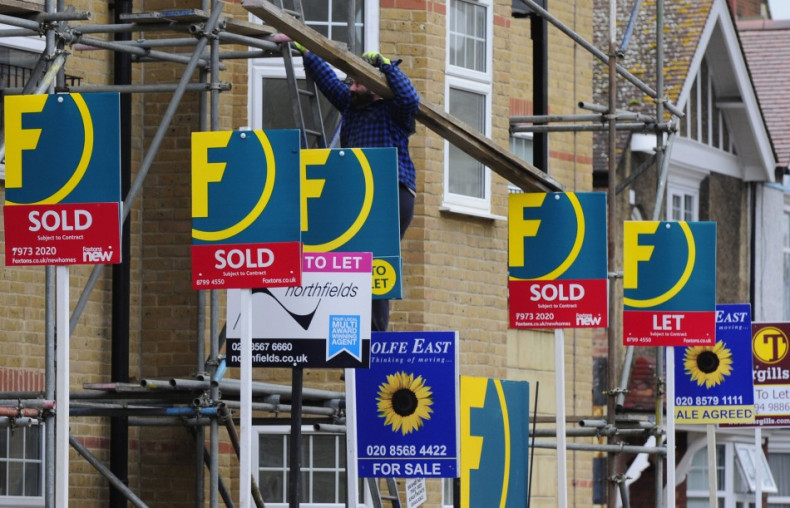 A man carries wood up scaffolding near For Sale and To-Let signs in west London