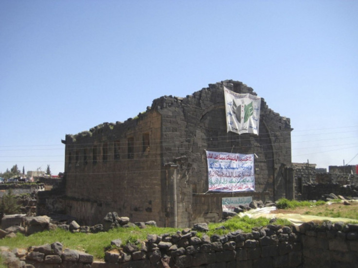 Demonstrators raise a banner, praising the Syrian Free Army battling Syrian President Bashar al-Assad along with verses from the Koran, on wall of Bosra's famous Roman ruins March 18, 2012. The ancient city structures have been damaged in the Syrian civil
