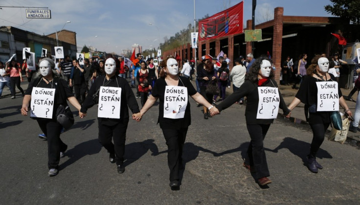 Demonstrators wearing masks and signs that read, "Where are they?" hold hands and walk during a protest marking the 1973 military coup in Santiago