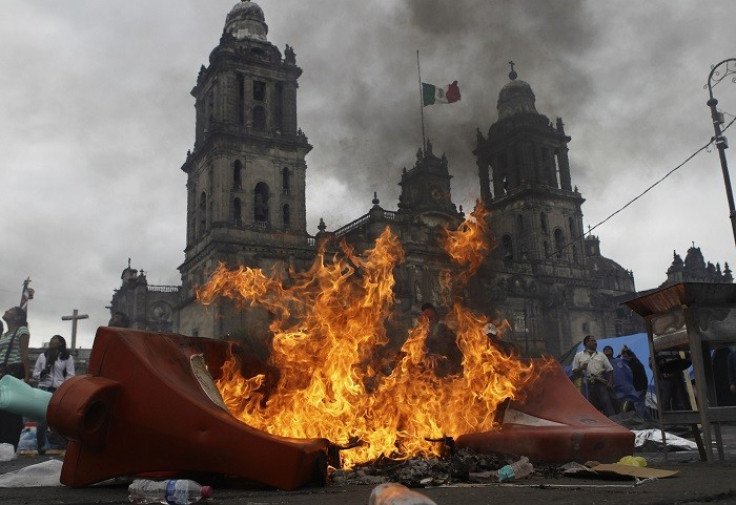 Teachers and protesters stand near a burning barricade before they are evicted from Zocalo Square by the riot police in Mexico City.