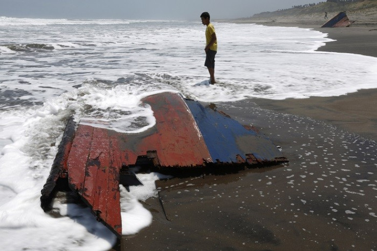A youth stands near a piece of wreckage of a boat which sank off the Indonesian coast
