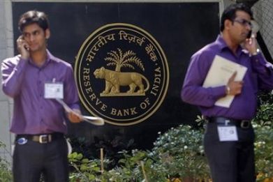 Two men make phone calls while standing near a Reserve Bank of India (RBI) crest at the RBI headquarters in Mumbai January 29, 2013.