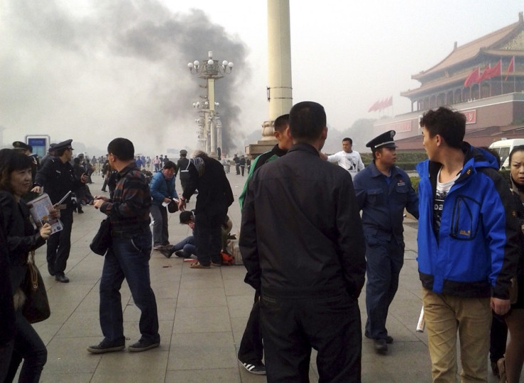 People walk along the sidewalk of Chang'an Avenue as smoke raises in front of the main entrance of the Forbidden City at Tiananmen Square