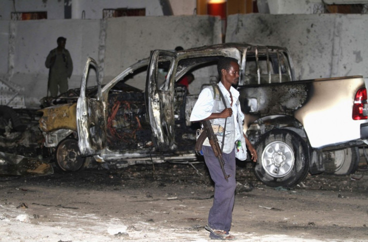 A Somali policeman walks past a burnt car after an explosion outside the Maka Al-Mukarama hotel in Somalia's capital Mogadishu