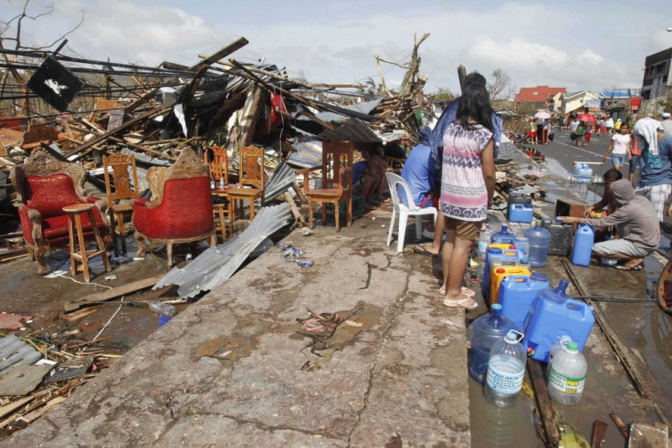 Survivors queue to get water from faucet near damaged houses