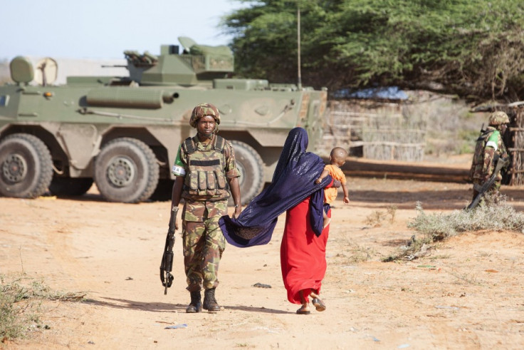 A woman walks by a Kenya Defence Force (KDF) soldier on the outer perimeter area of the Kismayu airport controlled by the African Mission in Somalia (AMISOM)