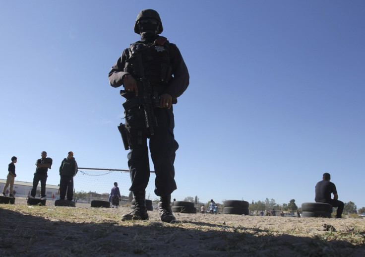 A police officer guards the perimeter of a house where a family was killed as neighbours play football in Ciudad Juarez