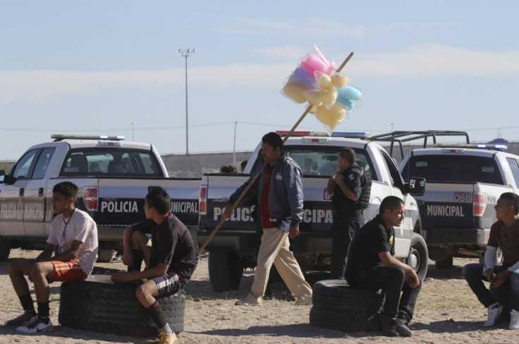 A man selling candy floss walks past patrol cars as a police officer guards the perimeter of a house where a family was killed in Ciudad Juarez