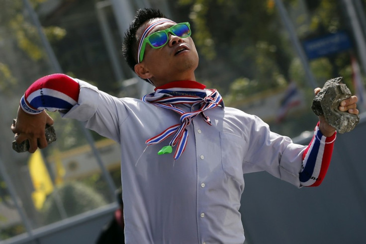 An anti-government protester wearing national colours throws a rock during clashes with police near the Government house in Bangkok