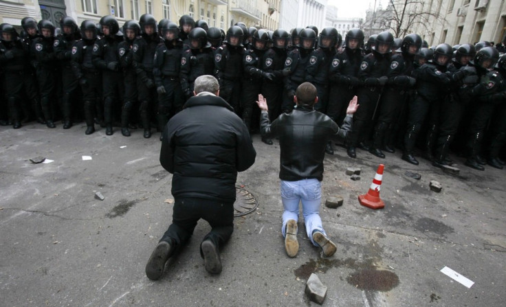 Men kneel down while riot police stand guard near the presidential administration building during a rally held by supporters of EU integration in Kiev