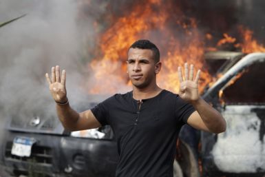 A pro-Mursi university student and supporter of the Muslim Brotherhood gestures with four fingers in front of a burning police vehicle at Al Nahda square in Cairo