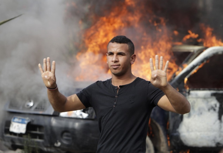 A pro-Mursi university student and supporter of the Muslim Brotherhood gestures with four fingers in front of a burning police vehicle at Al Nahda square in Cairo