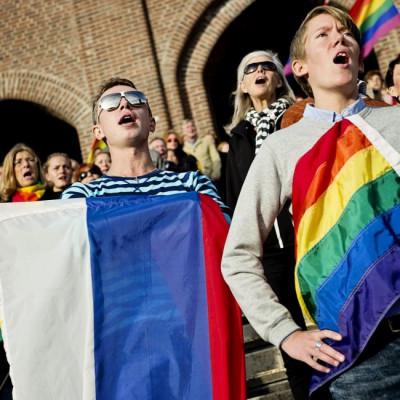 People sing the Russian national anthem while raising rainbow flags and a Russian flag (C) in solidarity with the lesbian, gay, bisexual and transgender (LGBT) community of Russia