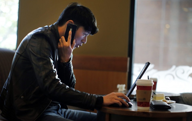 A man talks on the phone as he surfs the internet on his laptop at a local coffee shop in downtown Shanghai November 28, 2013. China's campaign against online rumours, which critics say is crushing free speech, has been highly successful in "cleaning