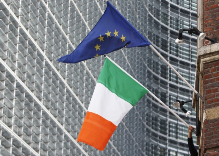 A man adjusts an Irish flag as it flies next to a European Union