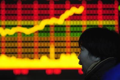 A woman looks at an electronic board with stocks information at a brokerage house in Hefei