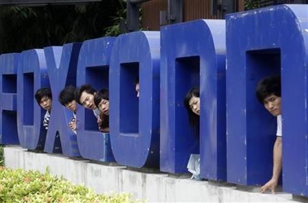 Workers look on from a Foxconn logo near the gate of a Foxconn factory in the township of Longhua, Guangdong province May 29, 2010.