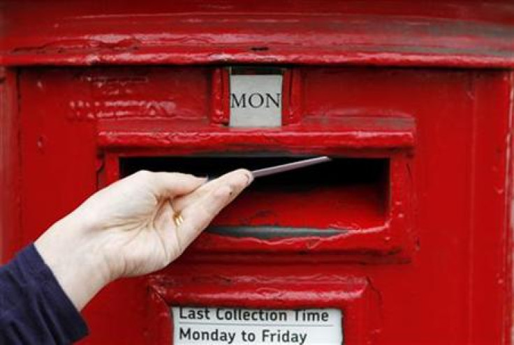 A woman posts a letter into a post box in south London